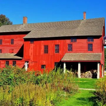Workers on cherry pickers and ladders painting the large red 1790 Laundry and Machine shop at the Hancock Shaker Village