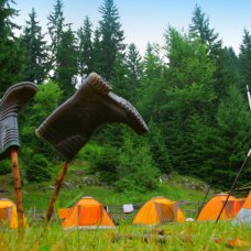 wellington boots drying on sticks near a campsite with orange tents