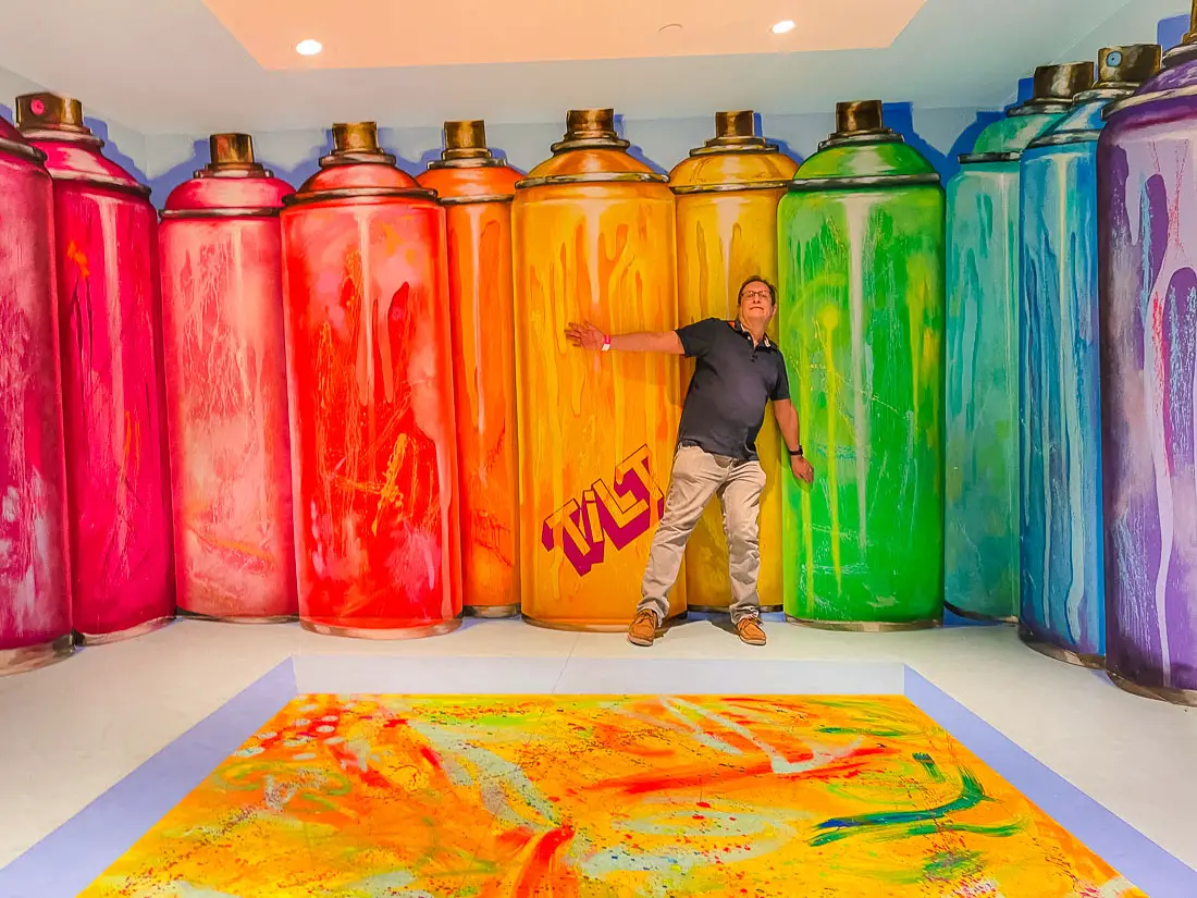 a mural of giant paint cans makes people appear smaller at the TILT Museum American Dream Mall